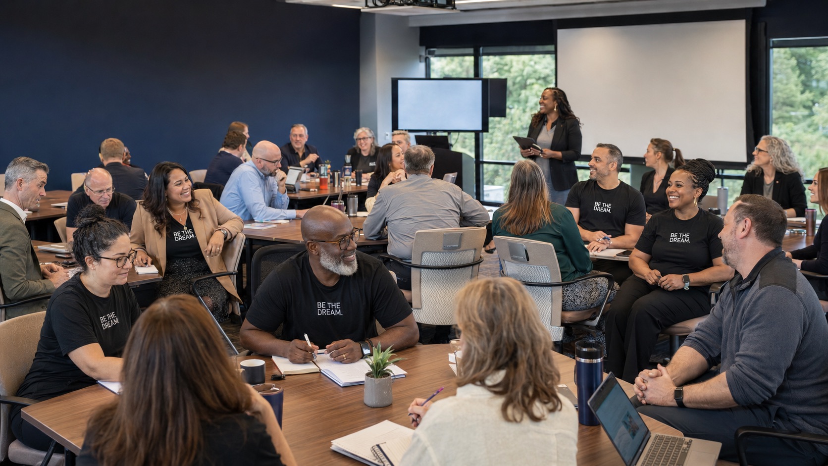 Adult educators and school leaders collaborating in a conference room, with several participants wearing BE THE DREAM T-shirts.